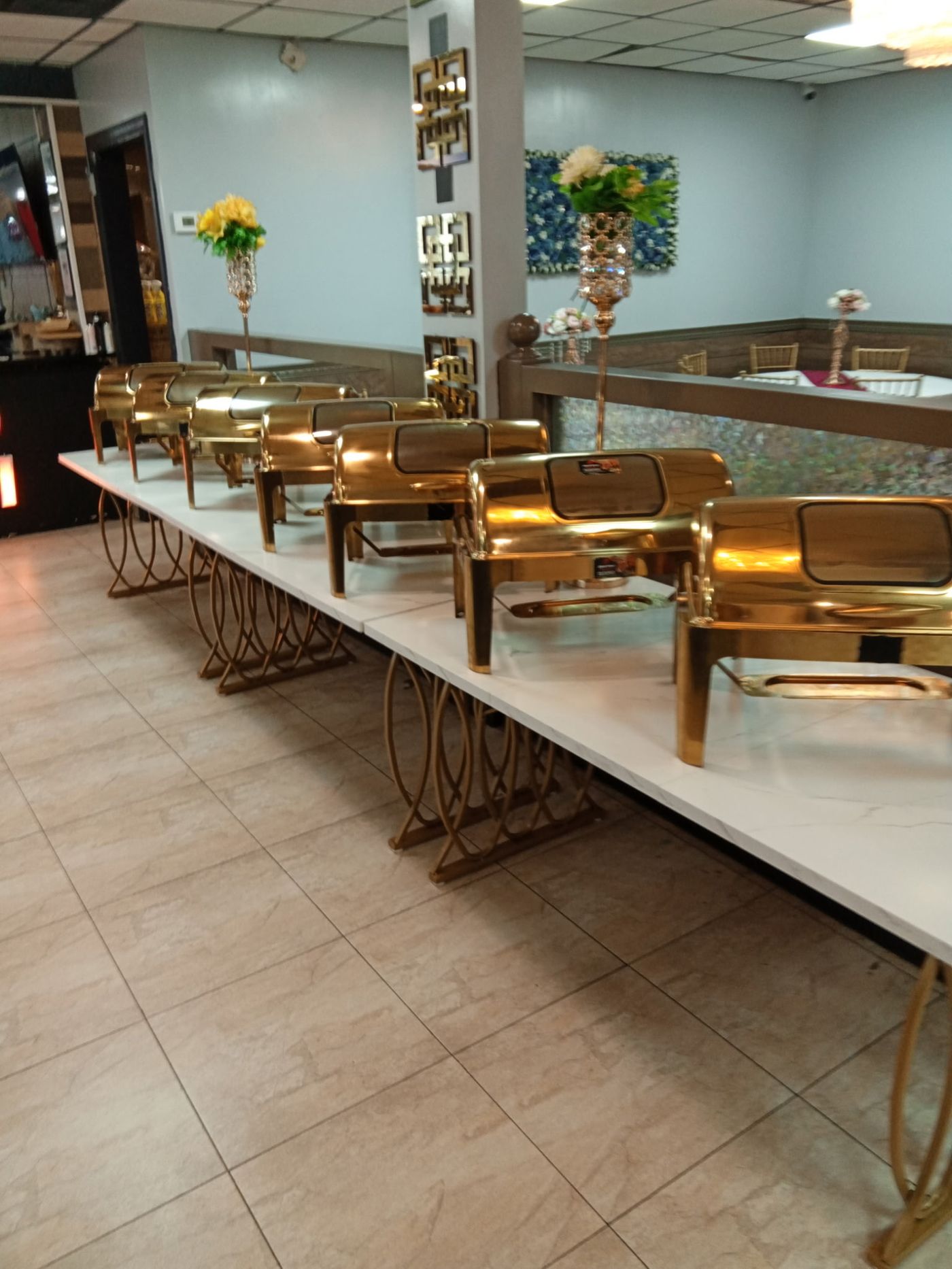 Gold chafing dishes lined up on marble-top buffet tables in a banquet hall